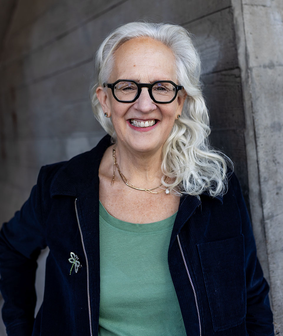 Image of Kate in a dark jacket and green t-shirt against a concrete wall background